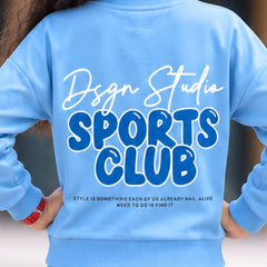 A person shown from the back wearing a light blue sweatshirt with a large graphic print reading 'Dsgn Studio SPORTS CLUB' and smaller text below, paired with matching light blue bottoms.