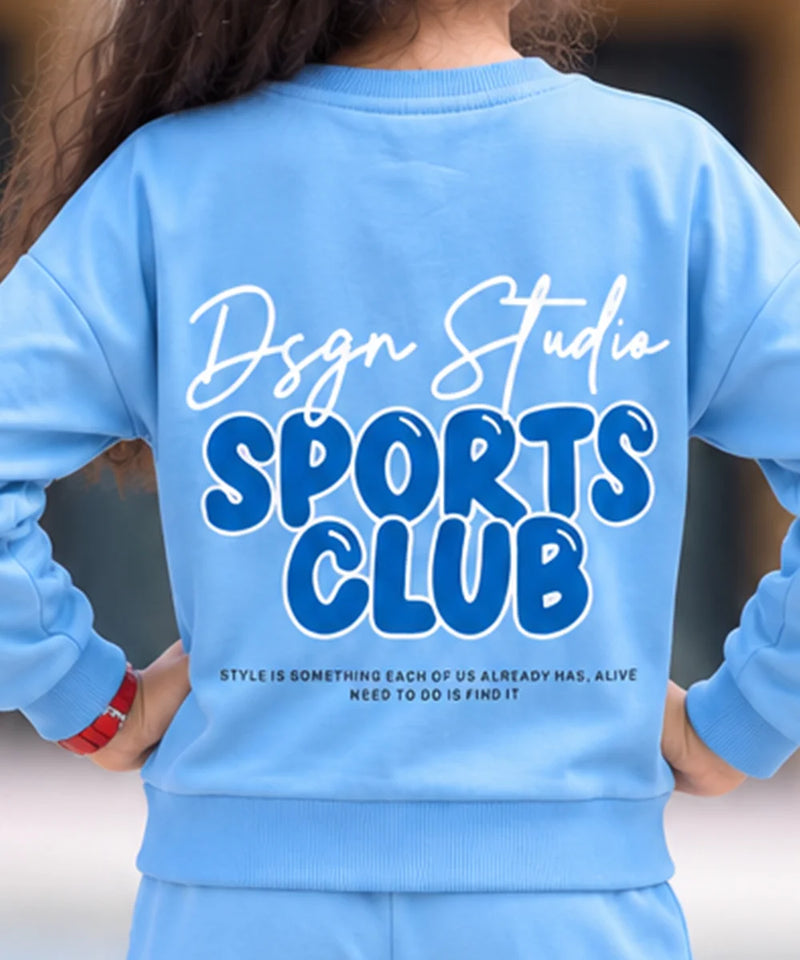 A person shown from the back wearing a light blue sweatshirt with a large graphic print reading 'Dsgn Studio SPORTS CLUB' and smaller text below, paired with matching light blue bottoms.