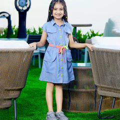 A girl wearing a blue denim party wear dress with long sleeves, standing on a grass-like surface with two large decorative seashells in the background.