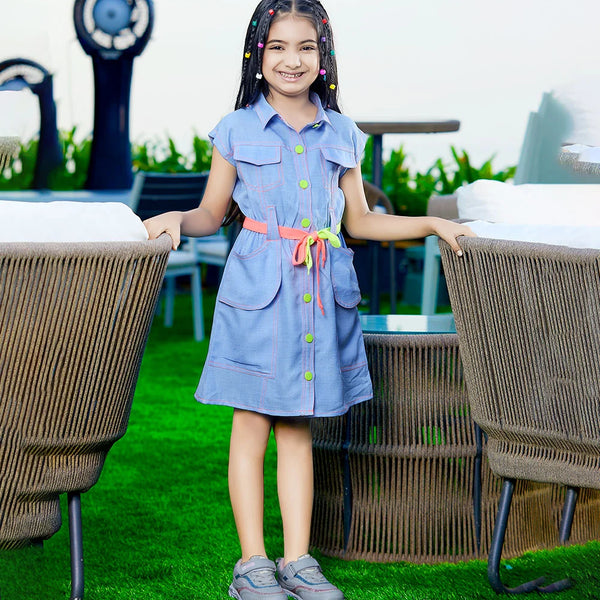 A girl wearing a blue denim party wear dress with long sleeves, standing on a grass-like surface with two large decorative seashells in the background.