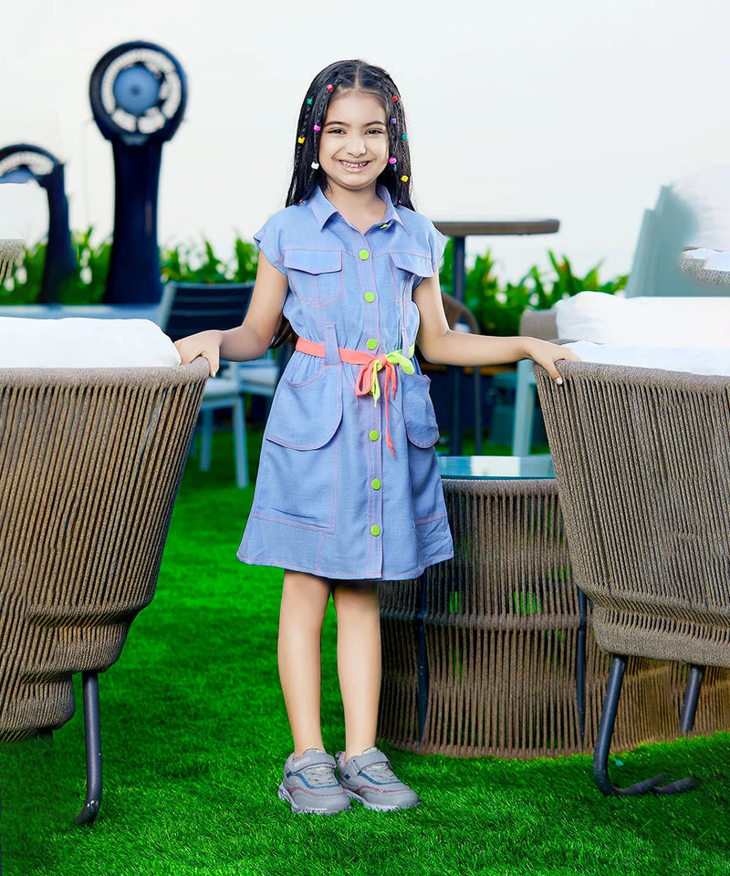 A girl wearing a blue denim party wear dress with long sleeves, standing on a grass-like surface with two large decorative seashells in the background.