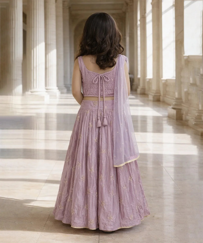 Woman in a lavender traditional outfit standing in a sunlit hallway.