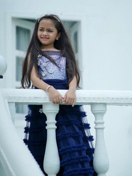 Young girl in a blue and purple dress sitting on a white railing.