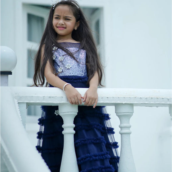 Young girl in a blue and purple dress sitting on a white railing.