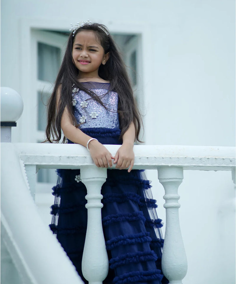 Young girl in a blue and purple dress sitting on a white railing.