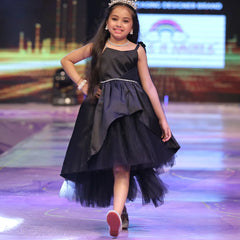 Young girl in a black dress with a tiara walking on a runway.