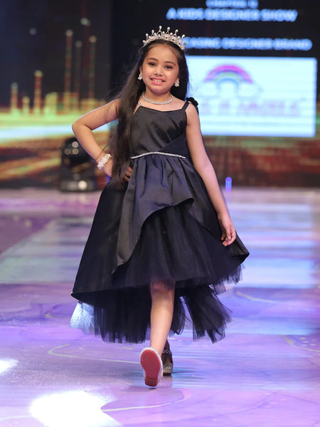 Young girl in a black dress with a tiara walking on a runway.