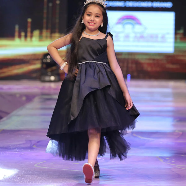 Young girl in a black dress with a tiara walking on a runway.