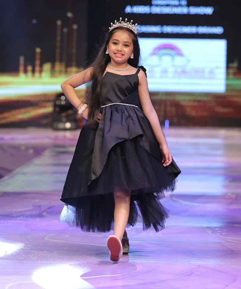 Young girl in a black dress with a tiara walking on a runway.