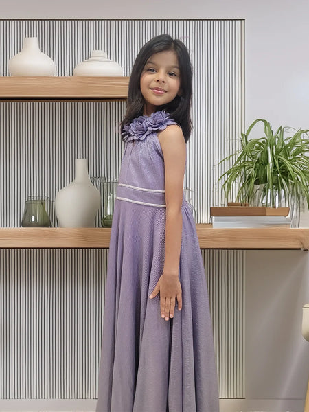 Young girl in a purple dress standing in front of a shelf with decorative items.