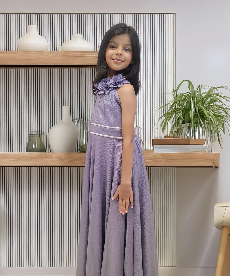 Young girl in a purple dress standing in front of a shelf with decorative items.