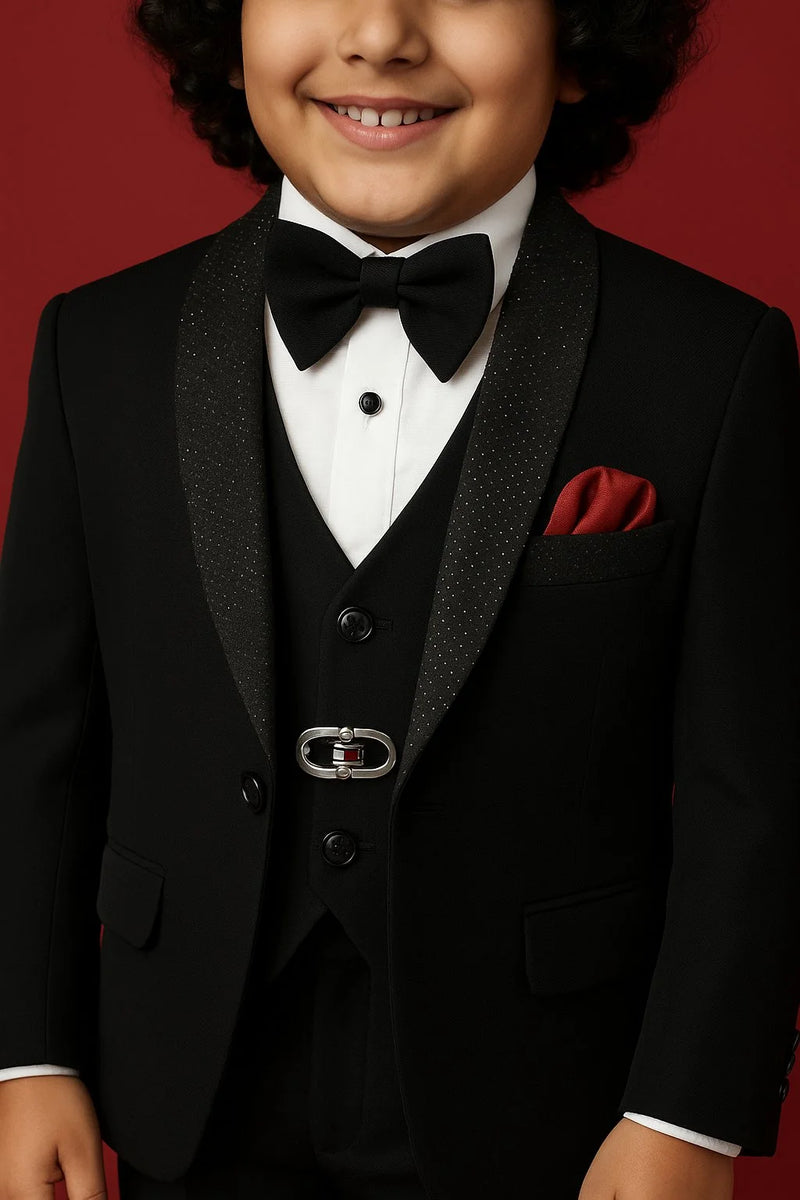 Child wearing a formal black tuxedo with a bow tie and red pocket square on a red background