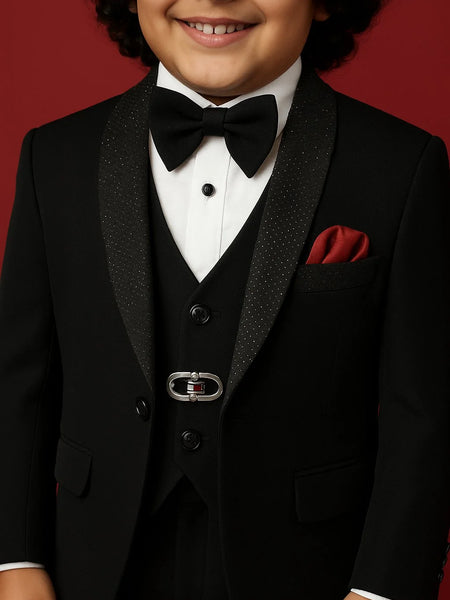 Child wearing a formal black tuxedo with a bow tie and red pocket square on a red background