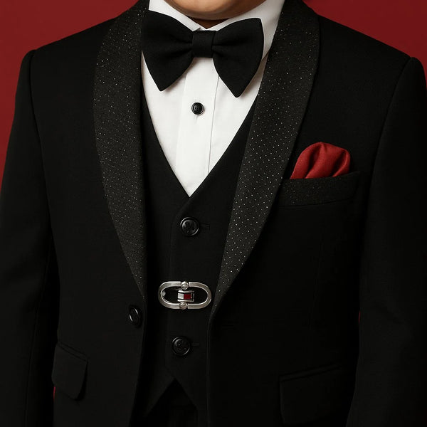 Child wearing a formal black tuxedo with a bow tie and red pocket square on a red background