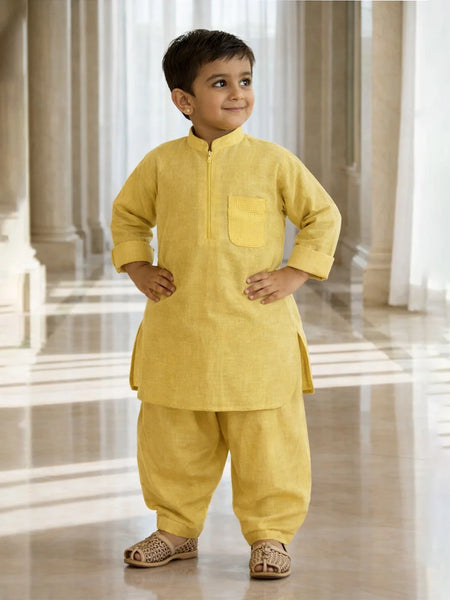 Child wearing a yellow traditional outfit standing in a bright, marble-floored room.
