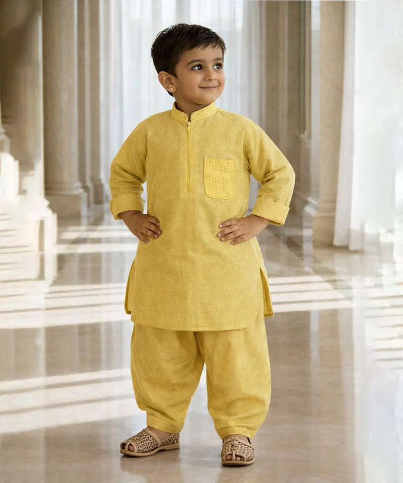 Child wearing a yellow traditional outfit standing in a bright, marble-floored room.
