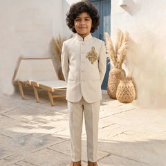 Child in a formal beige suit standing outdoors with decorative elements in the background