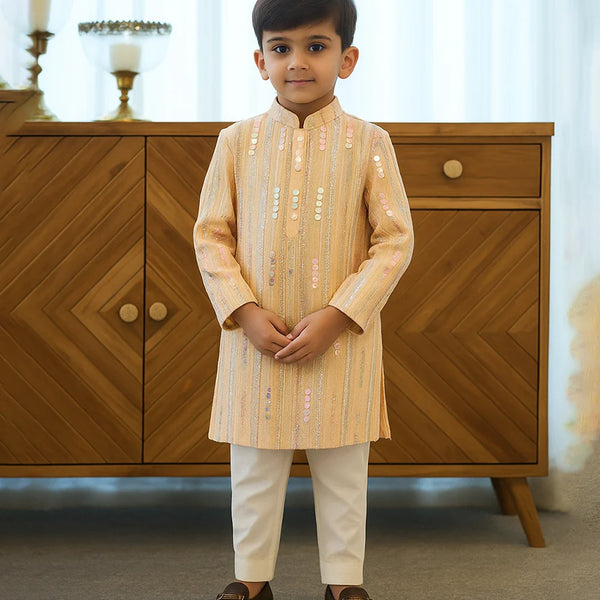 Young boy in traditional outfit standing in front of a wooden cabinet.