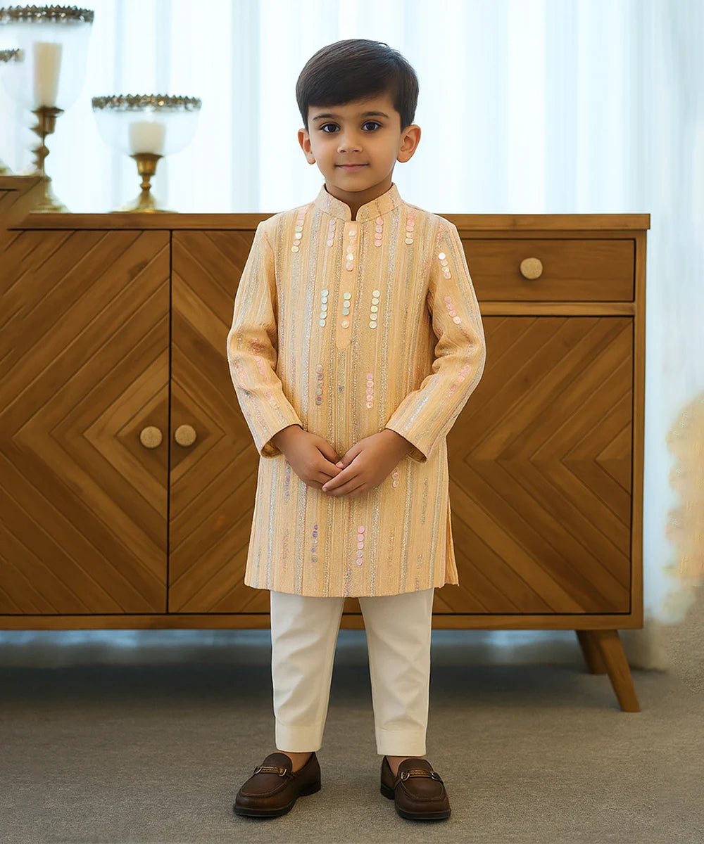 Young boy in traditional outfit standing in front of a wooden cabinet.