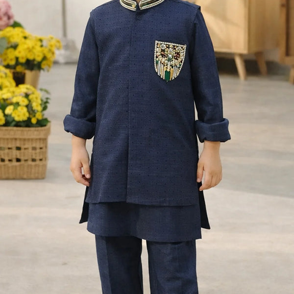 Child wearing a navy blue traditional outfit with decorative pocket, standing indoors.