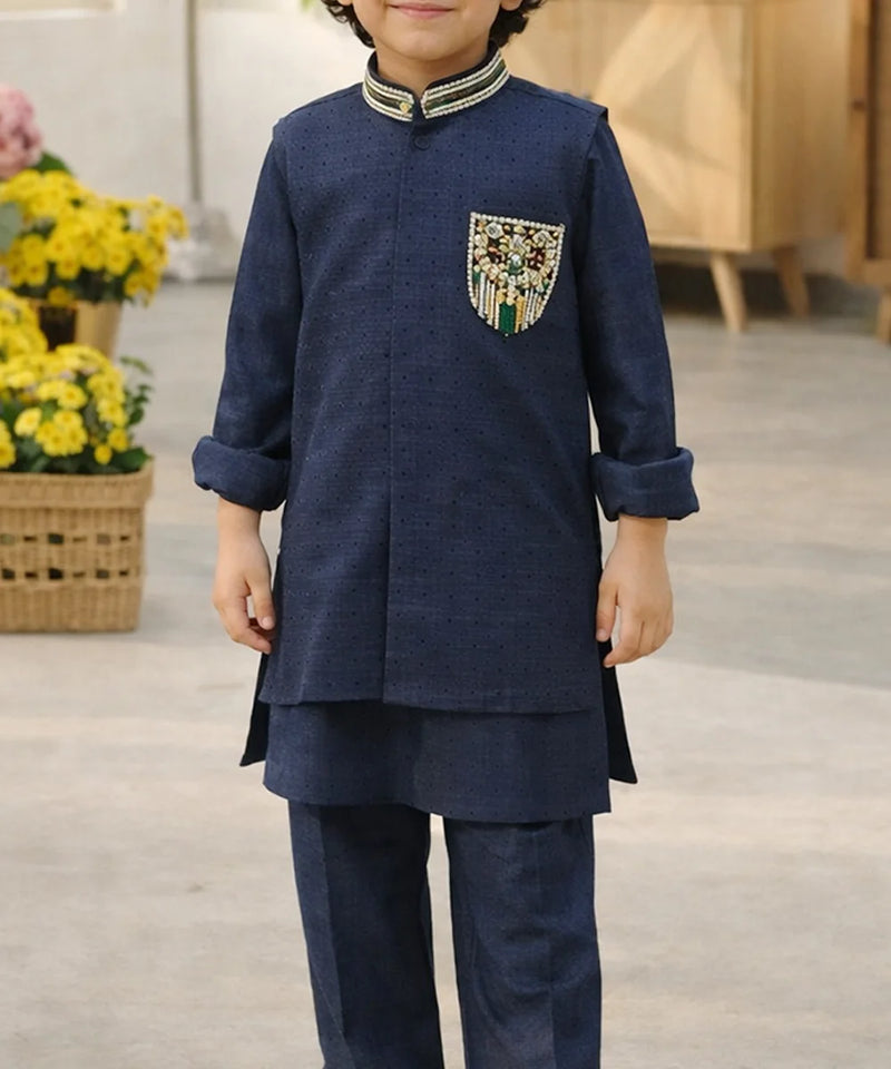Child wearing a navy blue traditional outfit with decorative pocket, standing indoors.