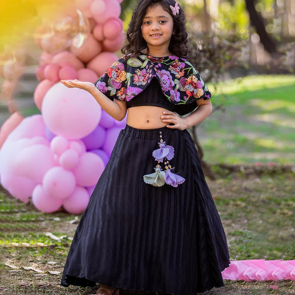 Young girl in a floral top and black skirt standing outdoors with balloons in the background