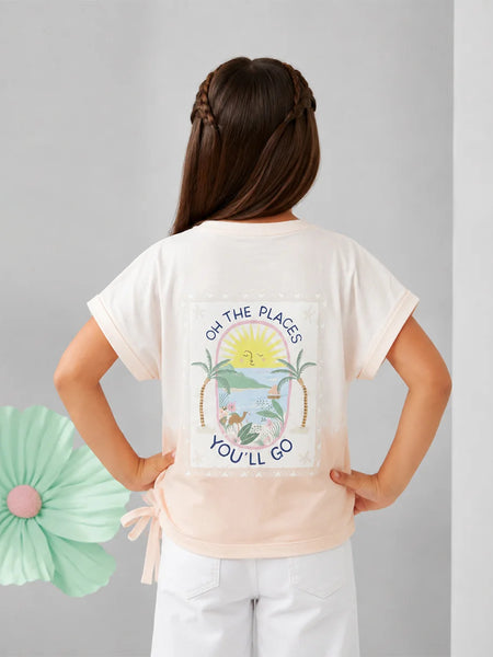 A young girl is shown from behind wearing a cream-colored t-shirt with a colorful tropical beach graphic and the text 'OH THE PLACE'S YOU'LL GO'. She is paired with white pants against a neutral gray background with a decorative mint green paper flower on the left.