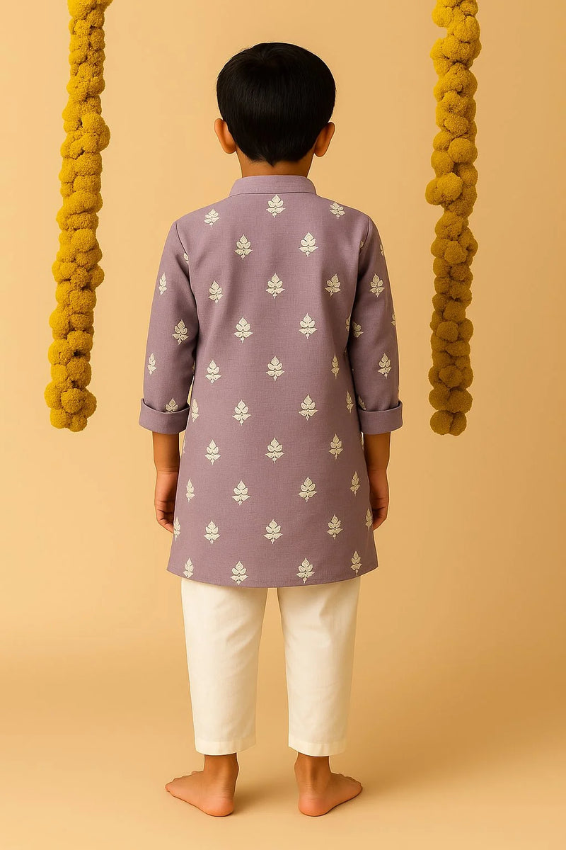 Child wearing a purple kurta with white patterns and white pants on a beige background