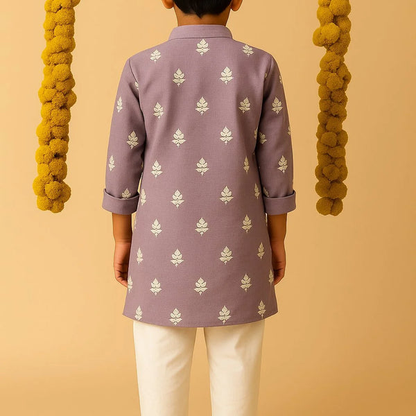 Child wearing a purple kurta with white patterns and white pants on a beige background