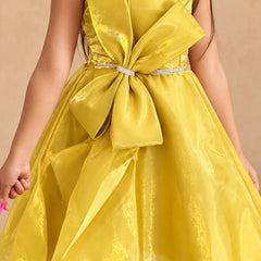 A bright yellow strapless dress with a large matching bow at the waist and a sparkly silver waistband, shown on a child against a plain beige background.