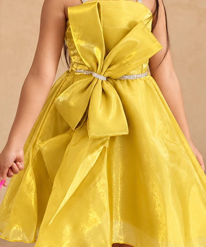 A bright yellow strapless dress with a large matching bow at the waist and a sparkly silver waistband, shown on a child against a plain beige background.