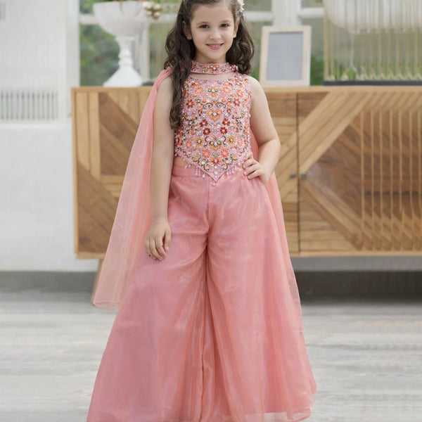 Young girl in a pink traditional outfit with floral embellishments indoors.