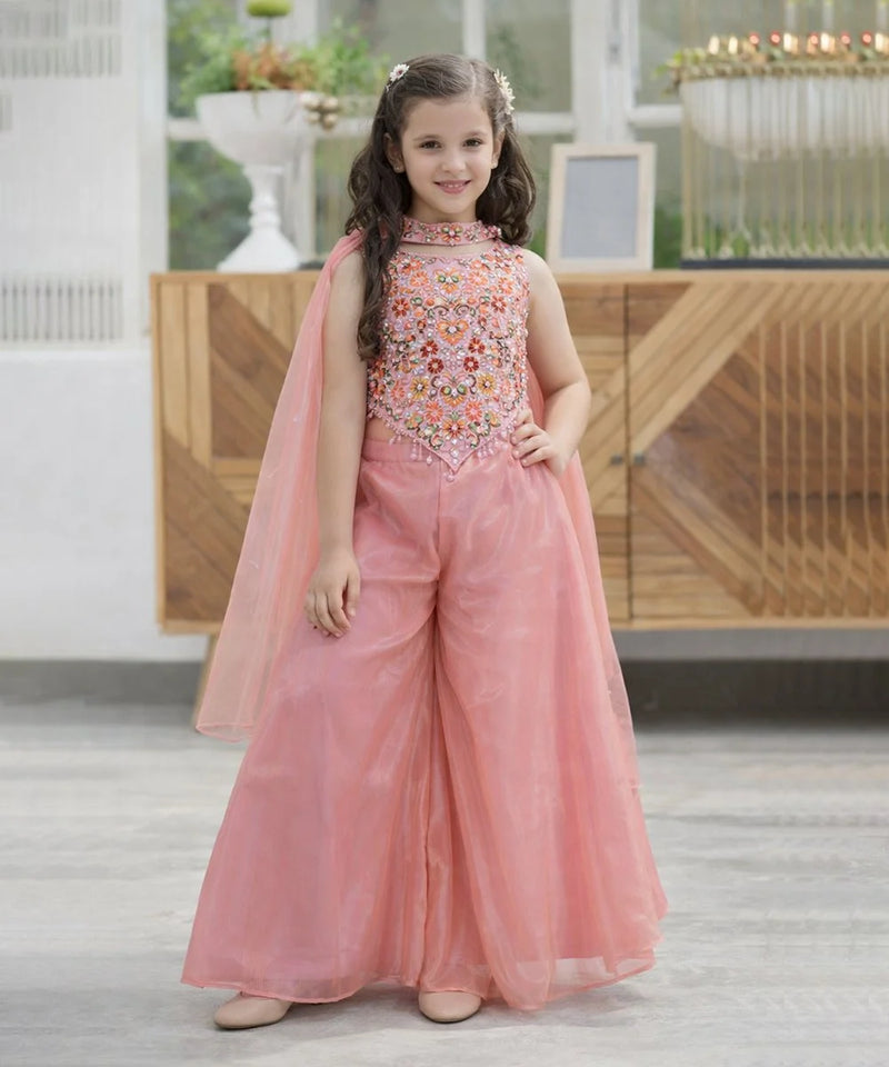 Young girl in a pink traditional outfit with floral embellishments indoors.