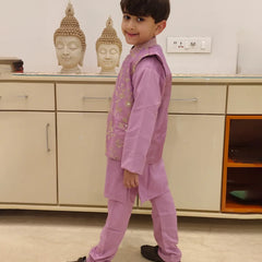 It is a side profile look of the boy wearing a lavender color kurta pajama with a gold thread embroidery.