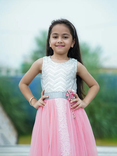 Young girl in a white top and pink skirt with a decorative brooch outdoors.