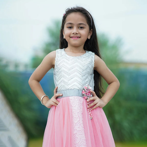 Young girl in a white top and pink skirt with a decorative brooch outdoors.