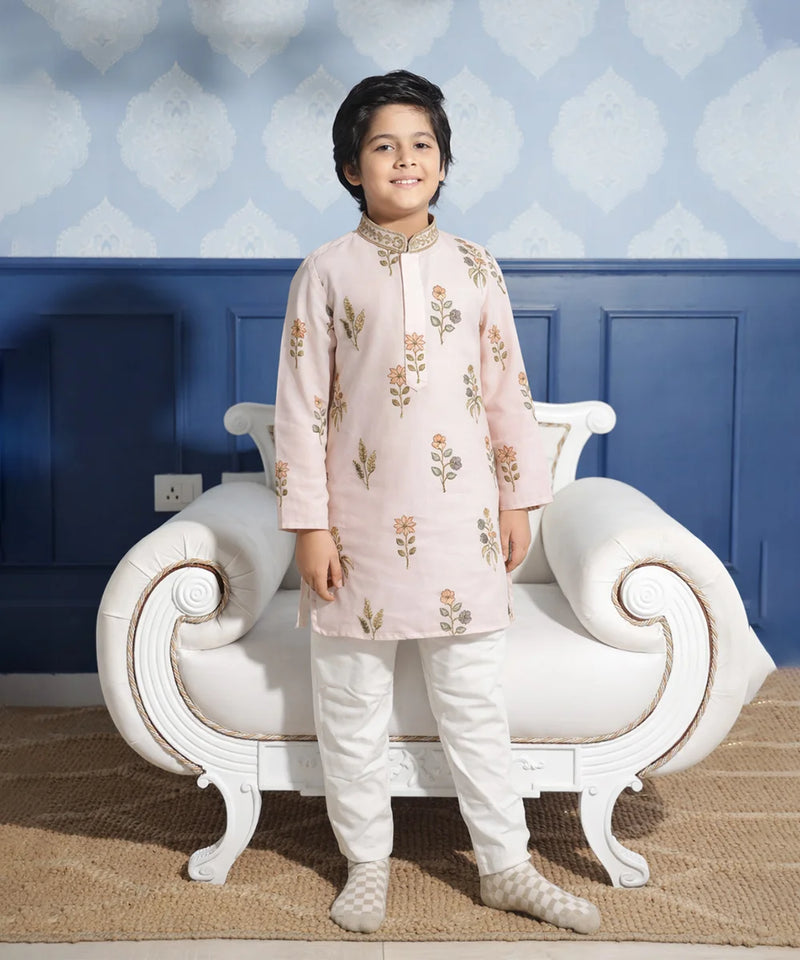 Child wearing a traditional outfit standing in front of a decorative chair with a blue wall background.