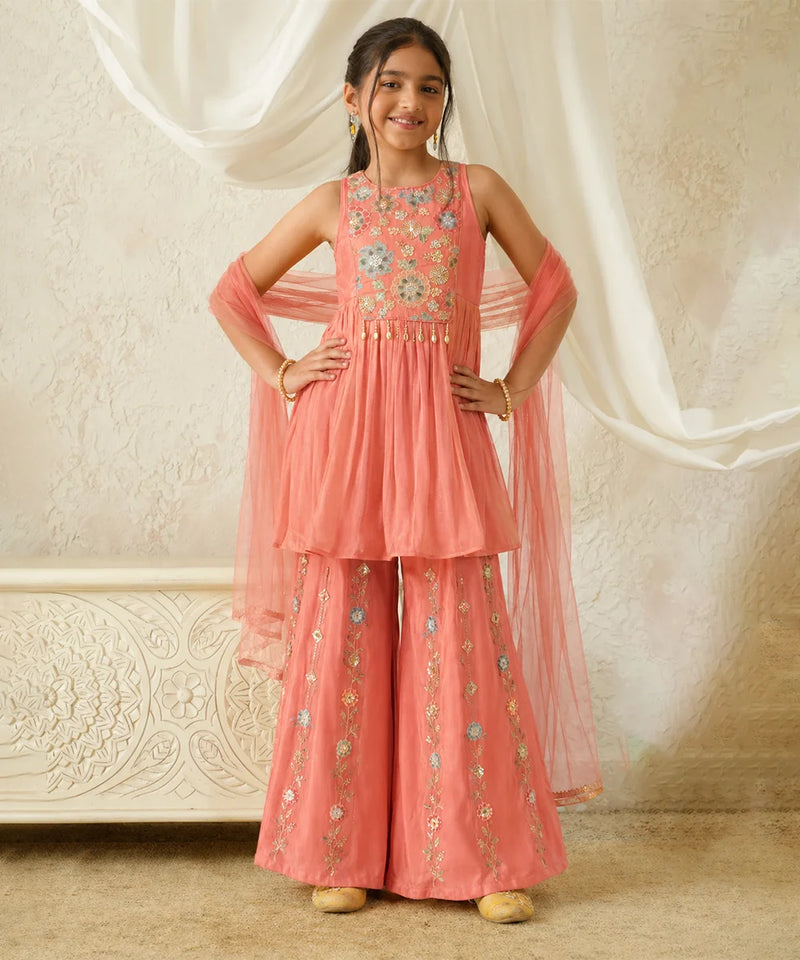 Young girl in a pink traditional outfit with floral embroidery against a white curtain background
