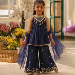 Young girl in a traditional navy blue outfit with gold details standing in a decorated room.