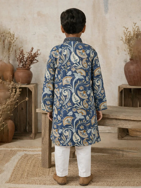 Child wearing a blue patterned kurta with white pants standing in a rustic indoor setting.