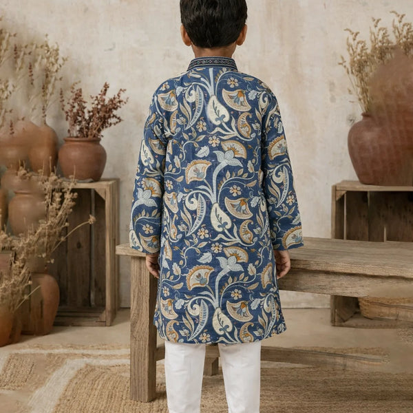 Child wearing a blue patterned kurta with white pants standing in a rustic indoor setting.