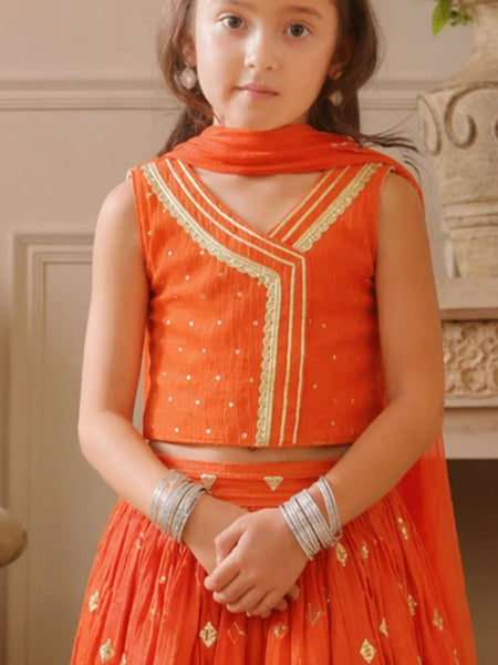 Young girl wearing an orange traditional outfit with gold embroidery indoors.