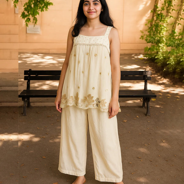 Woman in a cream-colored outfit standing outdoors with a bench and trees in the background