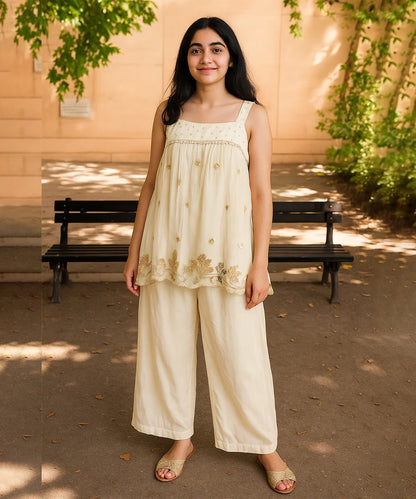 Woman in a cream-colored outfit standing outdoors with a bench and trees in the background