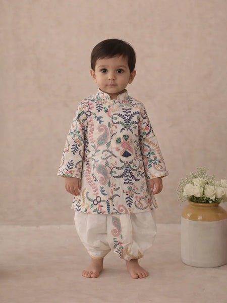 Child wearing a floral kurta with white pants standing against a plain background