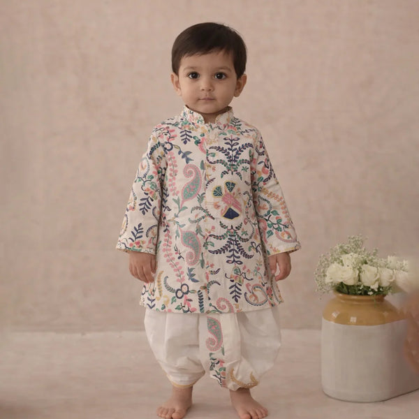 Child wearing a floral kurta with white pants standing against a plain background