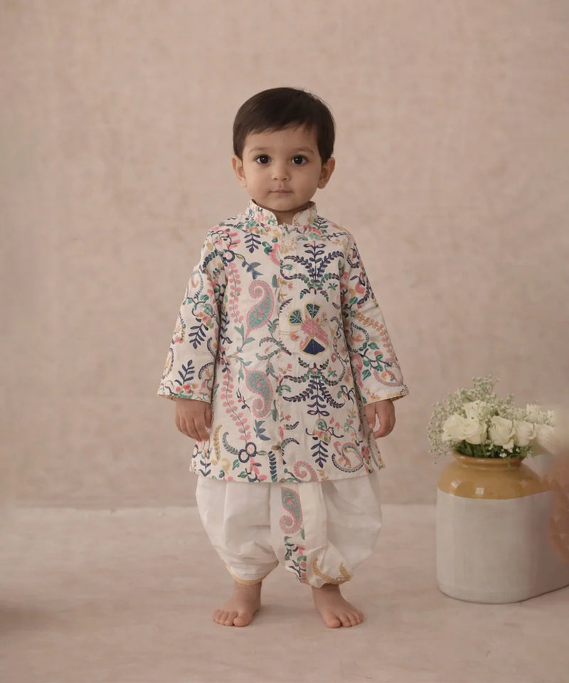 Child wearing a floral kurta with white pants standing against a plain background