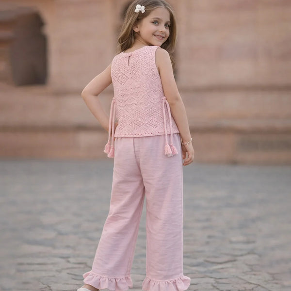 Young girl in a pink outfit standing on a stone pavement.