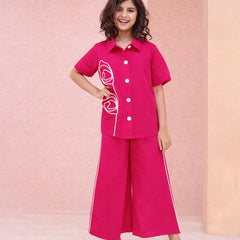 Young girl wearing a pink outfit with white buttons and trim against a pink background