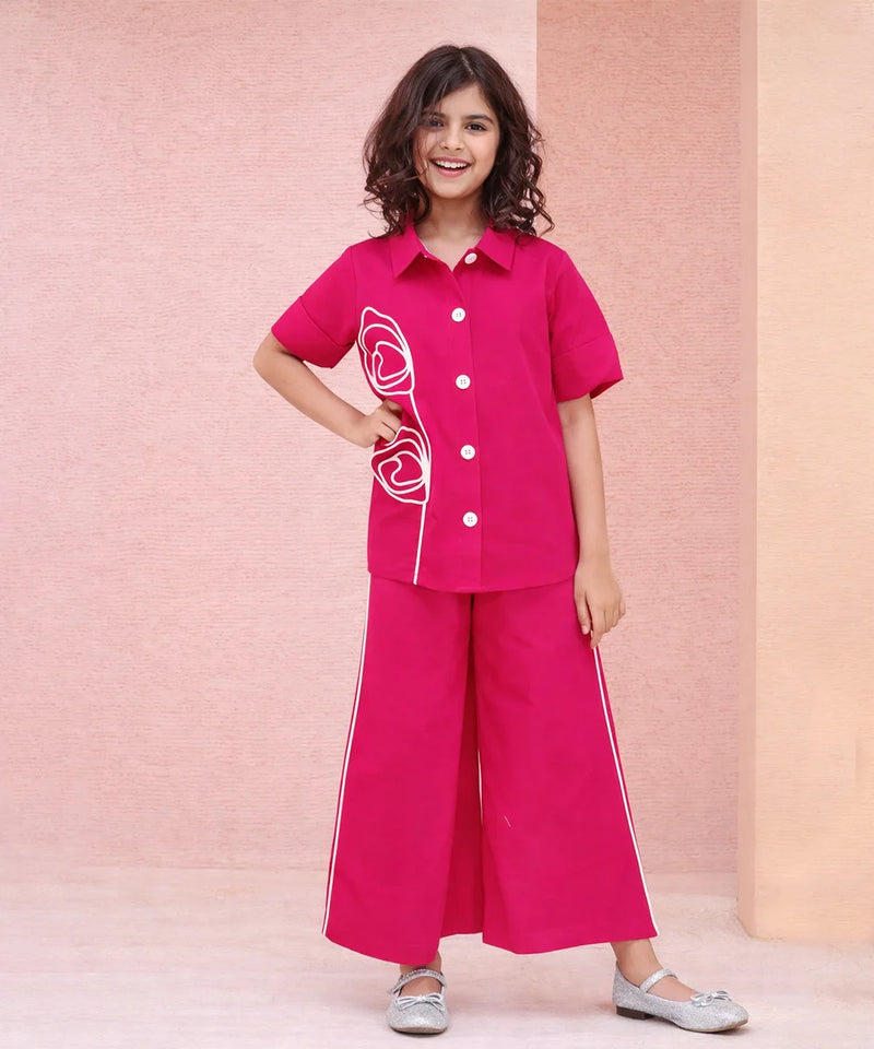 Young girl wearing a pink outfit with white buttons and trim against a pink background